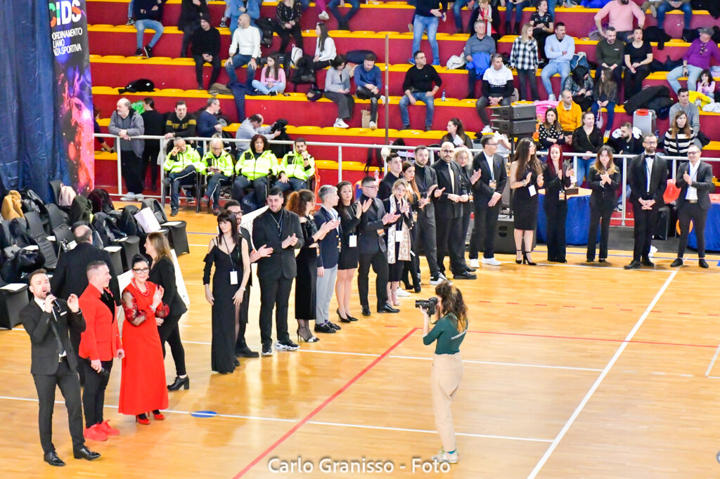 Giudici e staff della competizione in piedi mentre salutano il pubblico e gli atleti. Descrizione: Lo staff e la giuria del 4° Union Dance Open si presentano al pubblico, pronti a valutare le performance in gara.